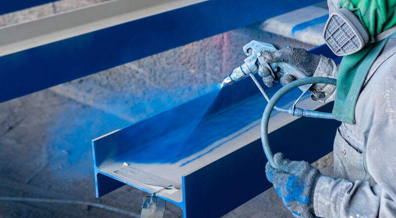 Auftragen einer Farbbeschichtung auf Stahlkonstruktionen mit einer Spritzpistole in einer Industrieanlage.