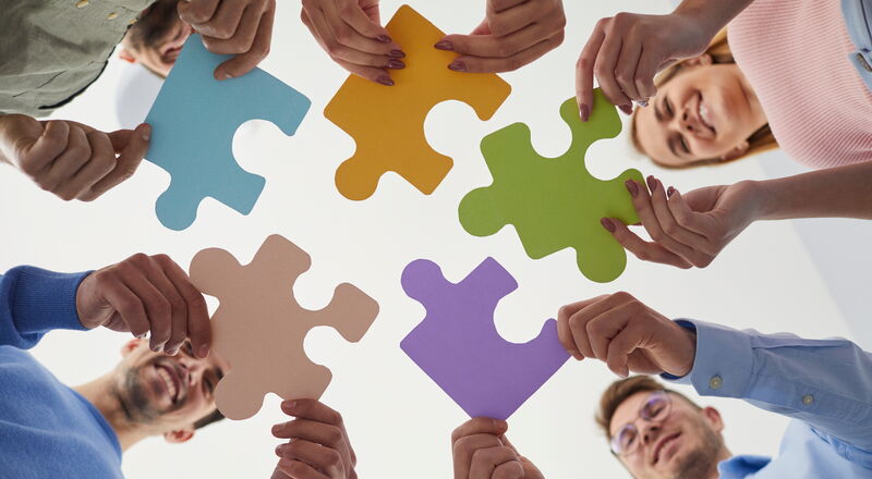 Junge Geschäftsleute halten Puzzles als Symbol für Zusammenarbeit, Problemlösung, kreatives Denken, Brainstorming und Teamarbeit in den Händen. Unterseite von lächelnden Menschen, die farbige Puzzleteile halten.